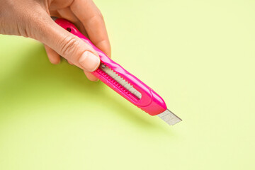Man with pink utility knife on green background, closeup