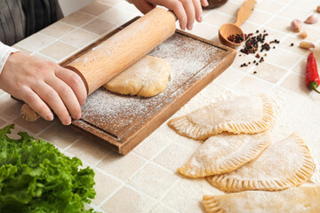 Woman rolling out dough for chebureks at table, closeup