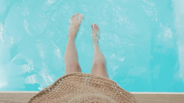 Beautiful sporty slim woman legs relaxing in water swimming pool spa, Enjoying suntan summer time, Female with hat splashing feet in turquoise blue waters, Vacation feeling concept, Top view