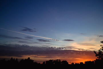 Fototapeta premium The morning glow illuminates the clouds on a beautiful colorful sky above the silhouettes of trees and a pillar at dawn
