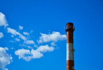 White and red boiler room chimney against the background of a beautiful blue sky and white clouds