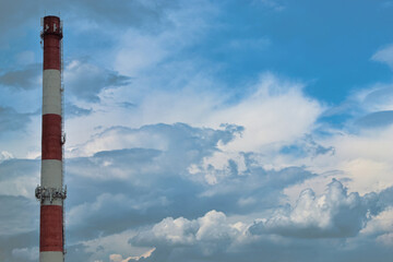 White and red chimney of the boiler house against the backdrop of a beautiful sky and thick cumulus clouds