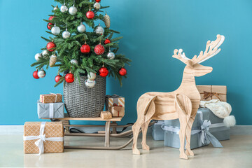 Wooden reindeer with sledge, Christmas tree and presents near blue wall