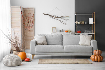 Interior of light living room with grey sofa, Halloween pumpkins and tree branches