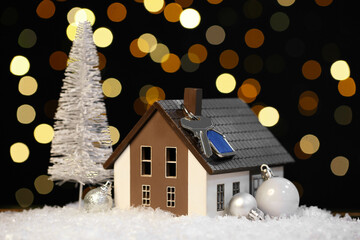 House model with key and Christmas decor on snow against blurred lights