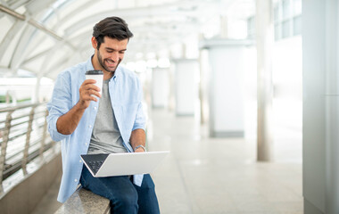 Young caucasian man holding cup of coffee and working on freelance project using portable computer at outer office.