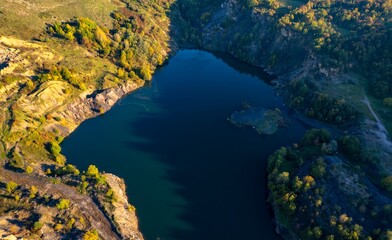 Fototapeta premium Aerial view of a small lake at sunset, that formed in a former coal mine exploitation, near Resita city, Romania. Captured with a drone, from above, in autumn setting. 