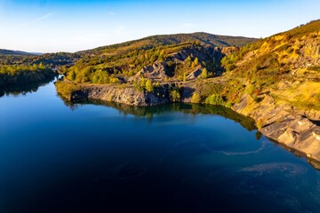 Fototapeta na wymiar Aerial view of a small lake at sunset, that formed in a former coal mine exploitation, near Resita city, Romania. Captured with a drone, from above, in autumn setting. 