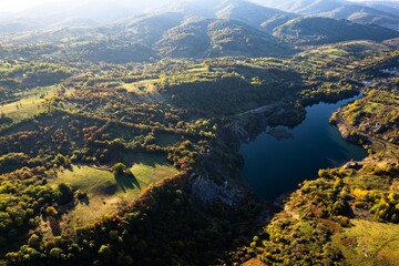 Aerial view of a small lake at sunset, that formed in a former coal mine exploitation, near Resita city, Romania. Captured with a drone, from above, in autumn setting.
