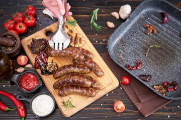 Grilled sausages and vegetables on wooden cutting board at domestic kitchen