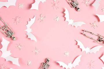 Halloween frame of white paper bats, skeletons and spiders on pastel pink background.