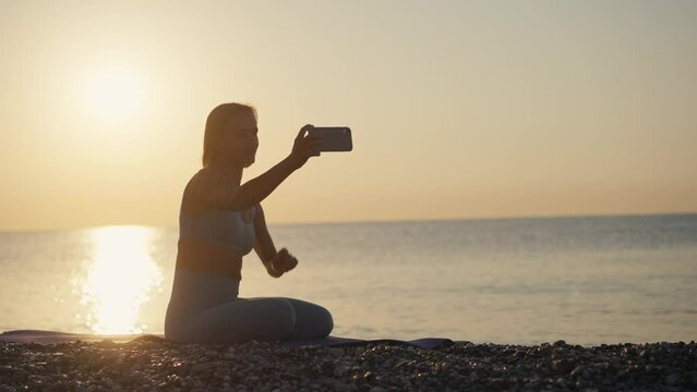 Smiling woman making selfie at sunrise on beach. Girl posing camera. Selfie after morning workout at sunrise.