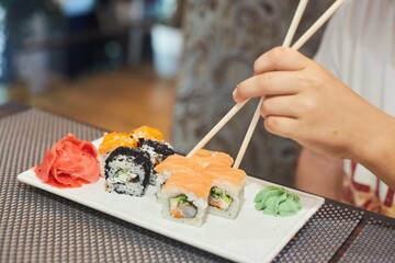 Assorted rolls on a plate and a hand with Japanese chopsticks. Several types of Japanese food from fish, vegetables and algae
