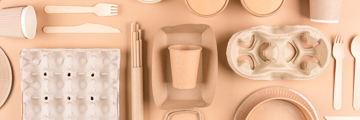 Banner. Sustainable paper packaging for food industry - paper utensils, cups, plates, drinking straws, egg boxes and food containers over light brown background. Flat lay