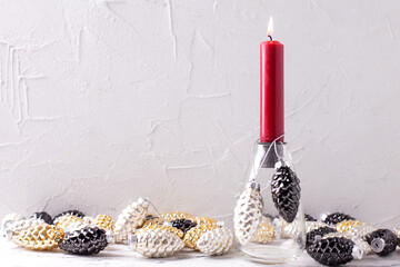 Background with Christmas decorations. Glass candleholder with gold, black, silver decorative cones...