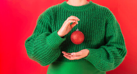 Women in a green sweater are holding the symbol of the New Year in their hands - a red Christmas...