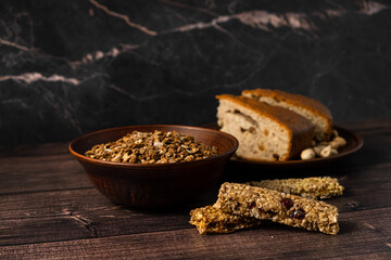 Energy breakfast. Chocolate granola with dried fruits in a bowl, various granola bars and a fruit pie on a dark background.