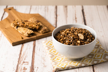 Energy breakfast. Chocolate granola with dried fruits in a bowl, various granola bars on a light wooden background.