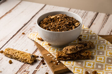 Energy breakfast. Chocolate granola with dried fruits in a bowl, various granola bars on a light wooden background.