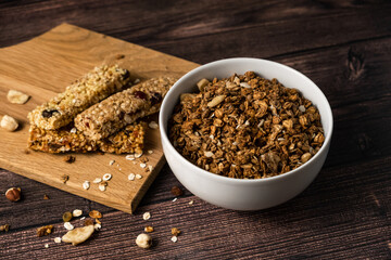 Energy breakfast. Chocolate granola with dried fruits in a bowl, various granola bars on a dark background.