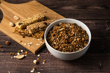 Energy breakfast. Chocolate granola with dried fruits in a bowl, various granola bars on a dark background.