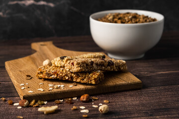 Energy breakfast. Chocolate granola with dried fruits in a bowl, various granola bars on a dark...