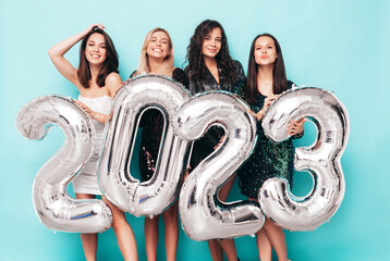 Beautiful women celebrating New Year. Happy gorgeous female in stylish sexy party dresses holding silver 2023 balloons, having fun at New Year's Eve Party. holiday celebration. Charming models