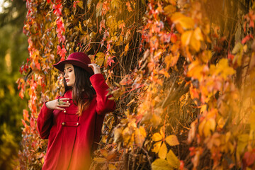 Fototapeta na wymiar Beautiful young woman in an elegant vintage outfit and a red hat against the background of wild grapes, autumn, October