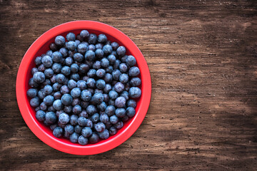 Blue plum in a red bowl on a wooden table. Small sweet fruit. Top view, place for text.