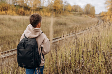 Rear view of teenager boy with backpack walking on path in autumn park. Active lifestyle, Back to...