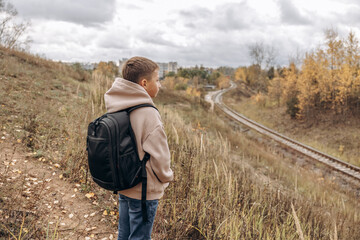 Naklejka na ściany i meble Rear view of teenager boy with backpack walking on path in autumn park. Active lifestyle, Back to school. Student boy in fall forest. People from behind