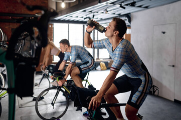 Sportsman drinking water training on stationary bike