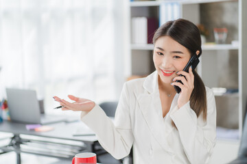 Young asian businesswoman beautiful charming smiling and talking on the mobile phone in the office