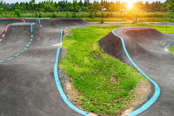 Off-Road Cycling Course.Asphalted bicycle pump track, racing speed track with traffic lines for  BMX racing track or Bicycle Motocross and Roller skating around with tree and sunlight background.