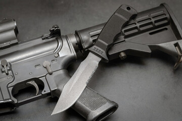 Fixed blade combat knife and assault rifle, close-up photo.