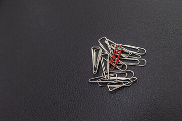Red paperclips among silver paperclips. Placed on the black leather upholstery.