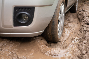 Close up shot of a car stuck in mud pool in the countryside. Dirt road after rains, mud on the road