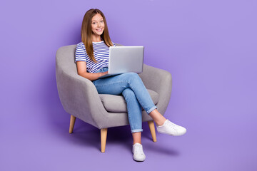 Full length photo of smart intelligent girl dressed striped t-shirt sit in armchair typing on laptop isolated on purple color background