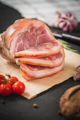 Spicy smoked ham with rosemary and kitchen knife on a black stone table. Pork roll