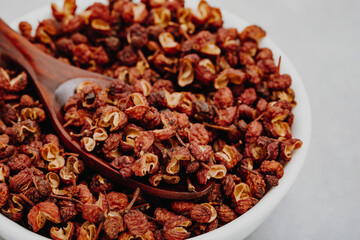 Sichuan pepper. Chinese pepper (Zanthoxylum schinifolium) in bowl on gray stone background close-up.
