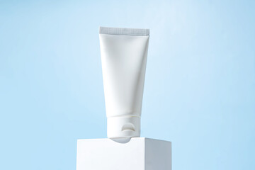 white cosmetic tube on a blue background on white cube. The concept of a cream with natural...