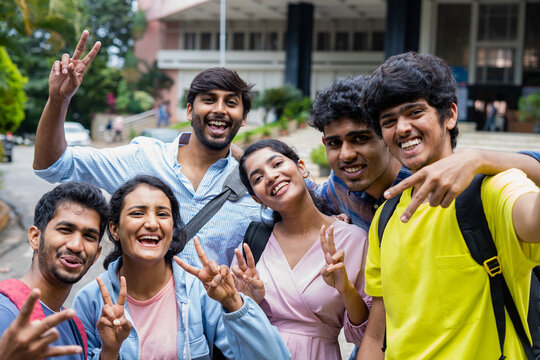 Group of smiling college students taking selfie by holding camera at college campus - concept of friendship, education and success.