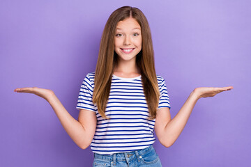 Photo of positive cheerful girl dressed striped t-shirt compare products demonstrating empty space isolated on purple color background