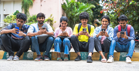 Group of indian college students busy using mobile phone at campus during leisure - concept of social media sharing, education and internet.