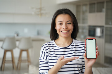 New mobile apps. Smiling female showing phone with mockup empty screen at home. Online store offer