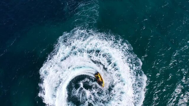Aerial drone top down video of jet ski watercraft performing circles showing off in high speed operated by stuntman in deep blue sea