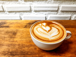 A cup of latte art coffee with tulip shape on old wooden desk and white brick background