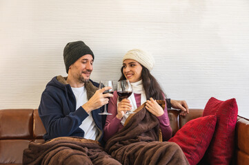 European couple smiling looking at camera in winter clothing holding glasses of red wine sitting on...