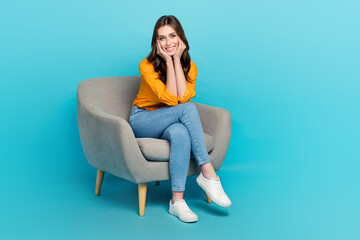 Full length portrait of gorgeous satisfied lad sit chair arms touch cheeks isolated on blue color background