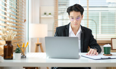 Concentrated male financial advisor using laptop and preparing contract document at office desk.